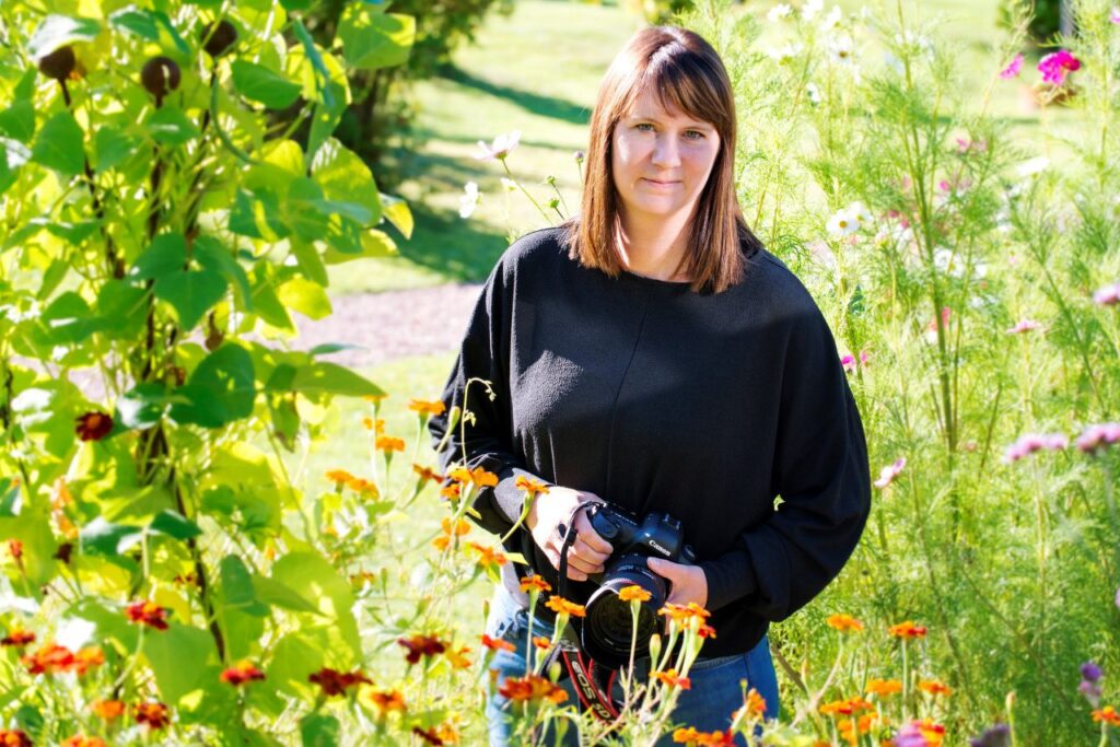 En kvinna som står bland grönskande träd och blommor